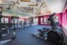 A modern gym in an apartment complex featuring treadmills, ellipticals, a weight rack, and various exercise equipment in a room with a colorful design and patterned ceiling.