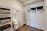 Apartment closet with organized shelving, storage bins, hangers, and a robe hanging against a white wall.