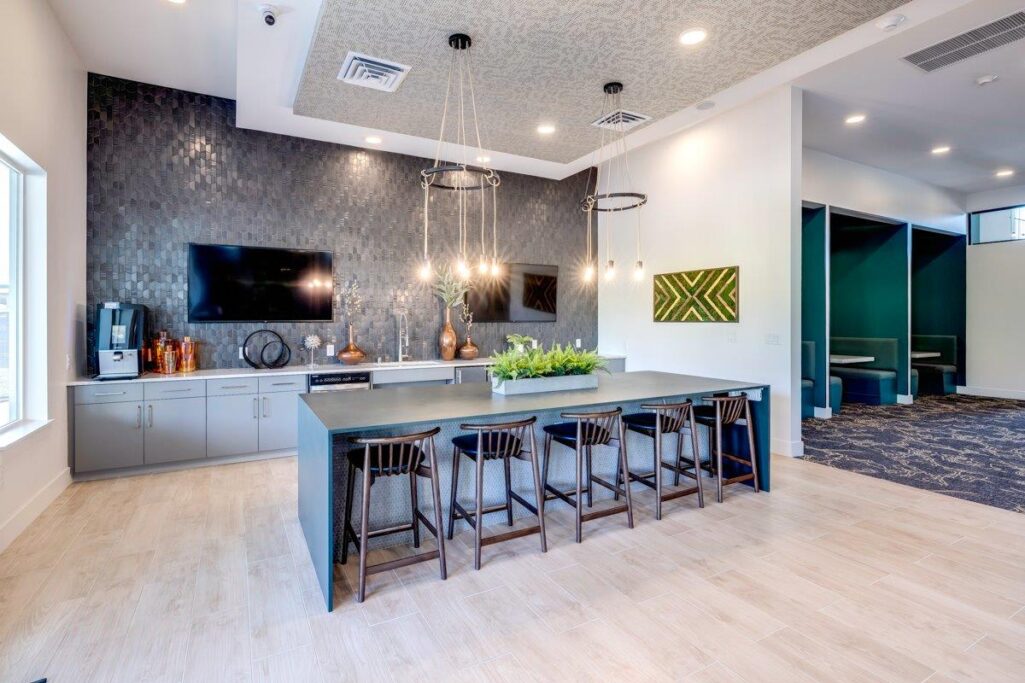 Modern community space with a kitchen area, dark cabinets, hanging lights, and a large counter with chairs.
