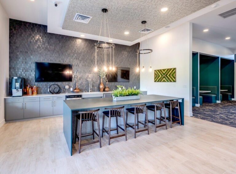 Modern community space with a kitchen area, dark cabinets, hanging lights, and a large counter with chairs.