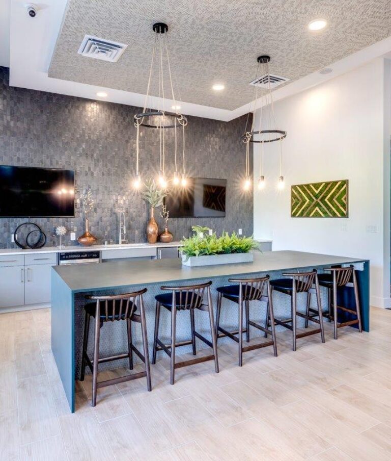Modern community space with a kitchen area, dark cabinets, hanging lights, and a large counter with chairs.