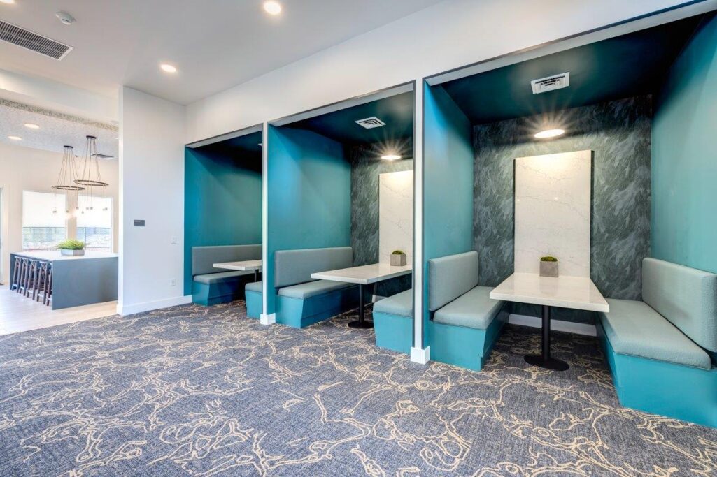 Modern community space with teal booth seating and a carpeted floor.