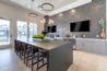 Modern community kitchen with a long table, bar stools, hanging lights, and wall-mounted TVs.