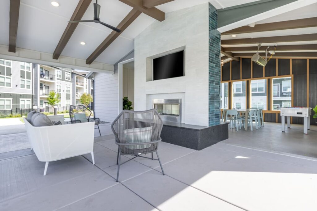 Modern apartment community space with outdoor seating, fireplace, and dining area.
