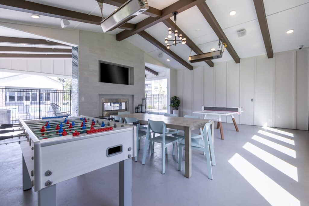 Apartment community space with a foosball table, dining table, fireplace, and TV.
