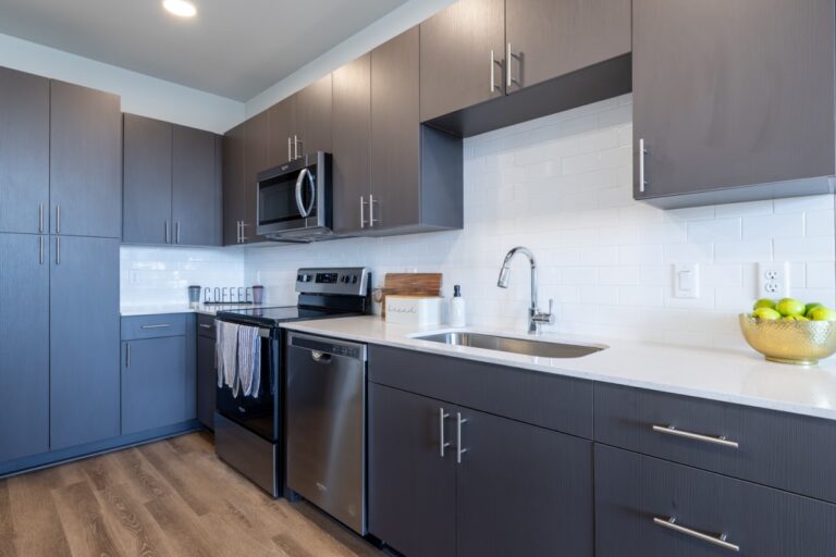 Modern kitchen in an apartment with sleek gray cabinets, stainless steel appliances, and a white tile backsplash.