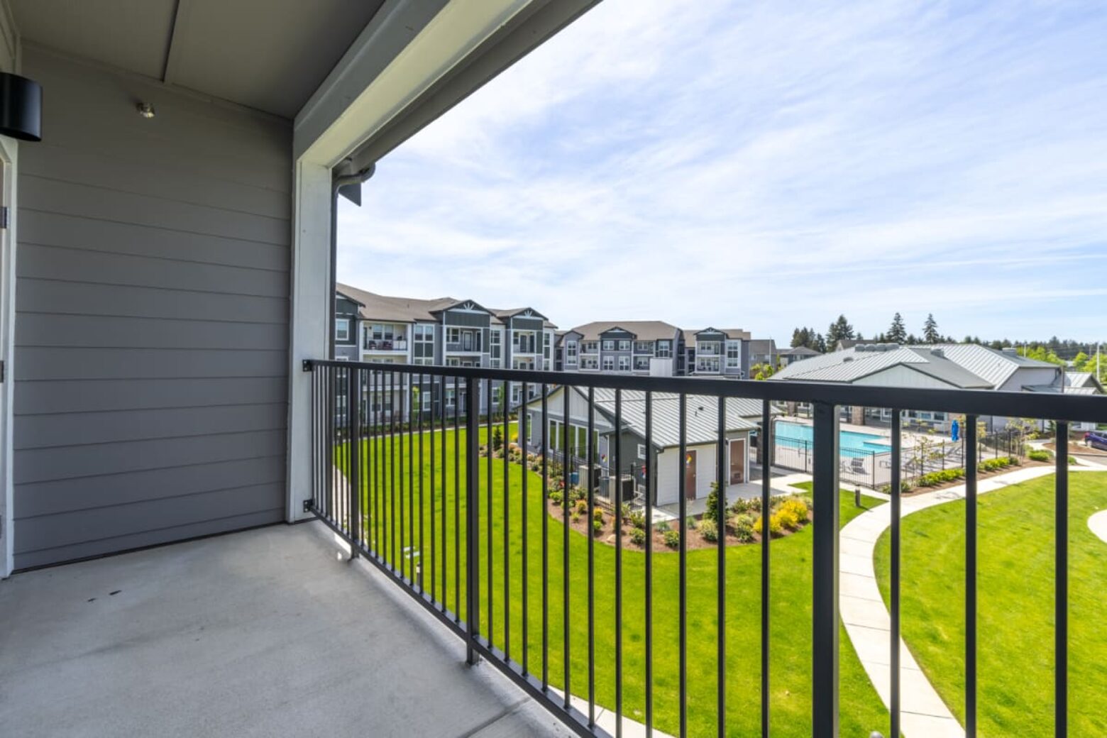 View from an apartment balcony overlooking a modern apartment complex with manicured green lawns and a swimming pool.