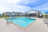 Outdoor swimming pool at Solace Rainer Ridge, surrounded by lounge chairs and blue umbrellas, with multi-story residential buildings in the background.
