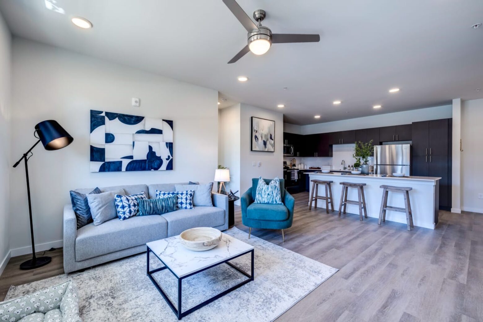 Modern apartment in Puyallup with an open-plan living room and kitchen, featuring a gray sofa, teal armchair, and bar stools at the kitchen island.